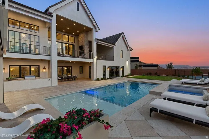 Modern home featuring an expansive resort-style backyard with an illuminated saltwater pool, integrated spa jets, and wide-plank paver decking