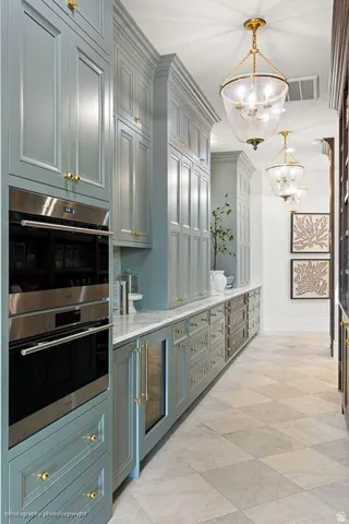 Full-height cabinetry, stainless steel double wall oven, integrated beverage cooler, light-toned countertop, and gold-finish hardware
