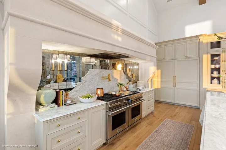 Gourmet kitchen featuring a large professional-grade range, custom cabinetry, paneled refrigerator, marble countertops, and light wood-finish flooring