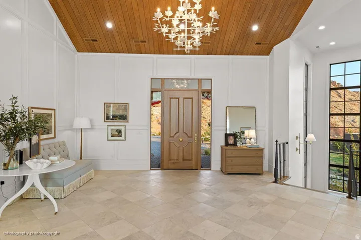 Spacious entry featuring a wood plank ceiling, decorative chandelier, paneled walls, and tiled flooring