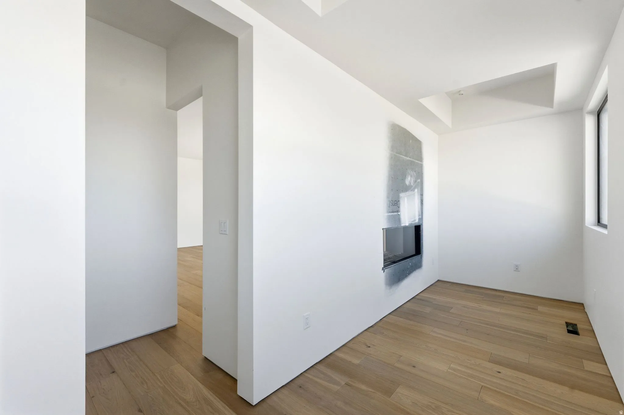 Wood-finish flooring, recessed fireplace, white walls, tray ceiling, and a window with dark trim