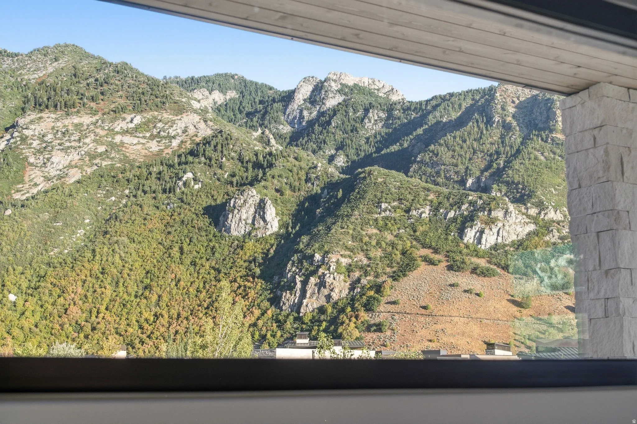 Expansive mountain scenery with abundant evergreen trees, a sleek window frame, and a stone-clad architectural element