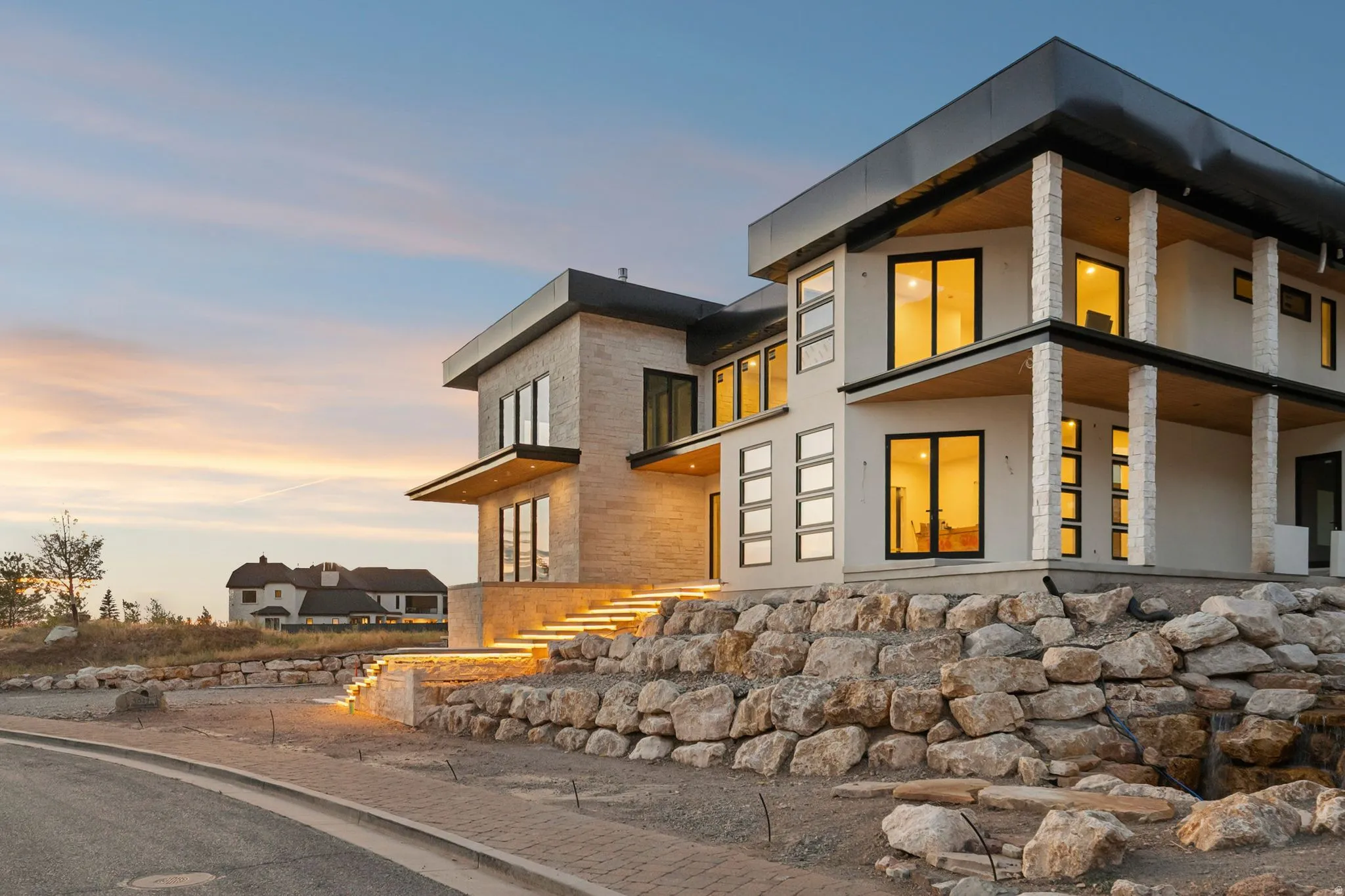 Modern architectural design featuring large windows, stone facade accents, layered rooflines, and illuminated exterior steps with integrated lighting