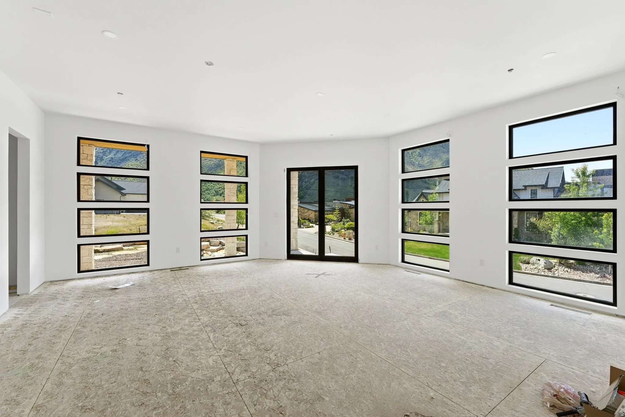 Expansive room featuring multiple full-height windows, a double glass door, recessed ceiling lighting, and a neutral color palette