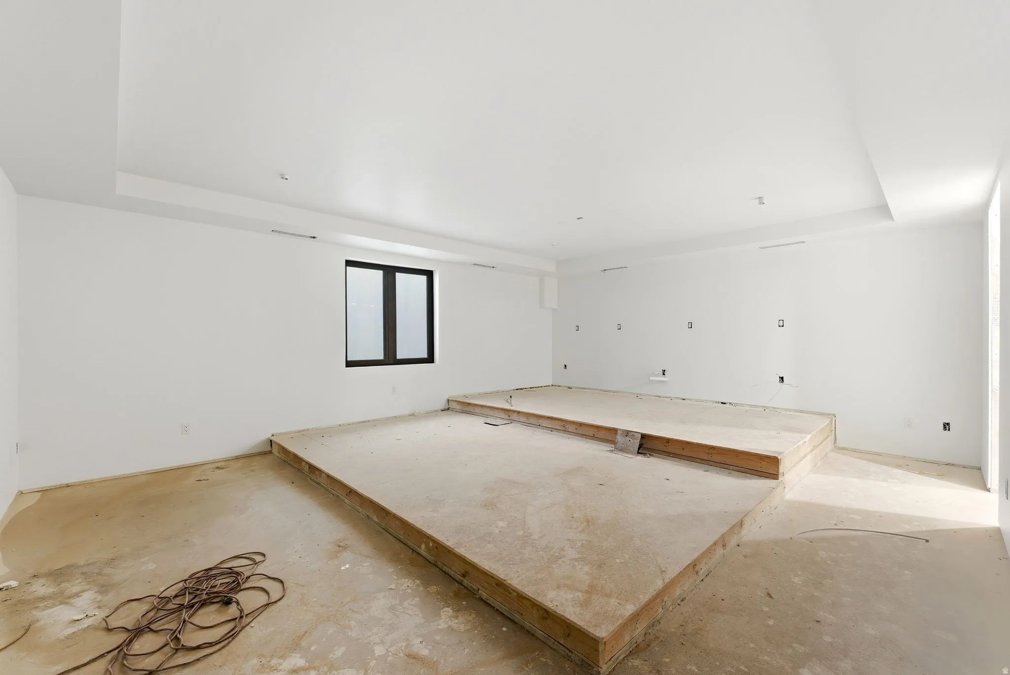 Spacious interior featuring a recessed ceiling, a multi-level platform, and a window with dark framing