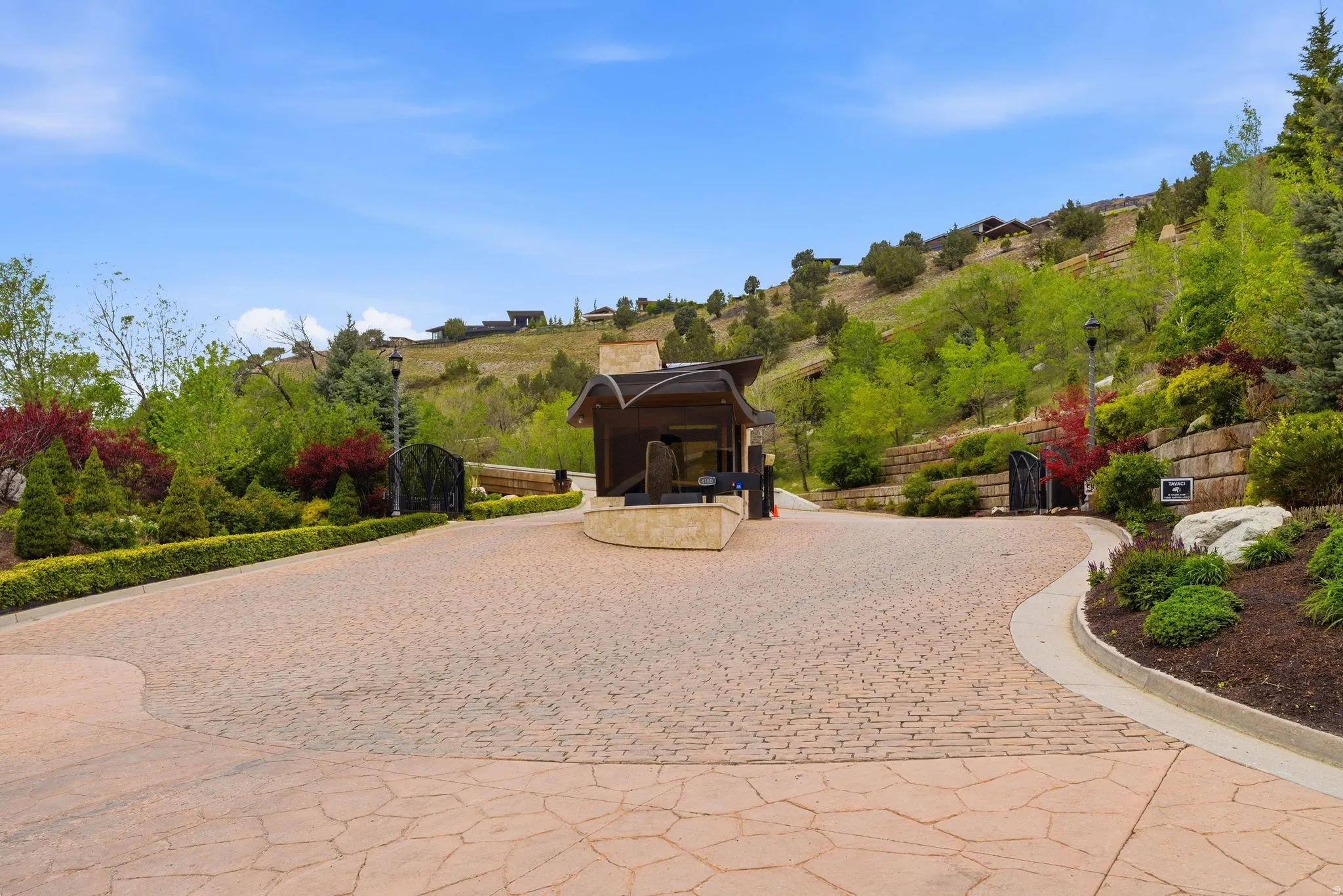 Stone paver driveway with integrated landscaping, gated entry, and a guardhouse structure