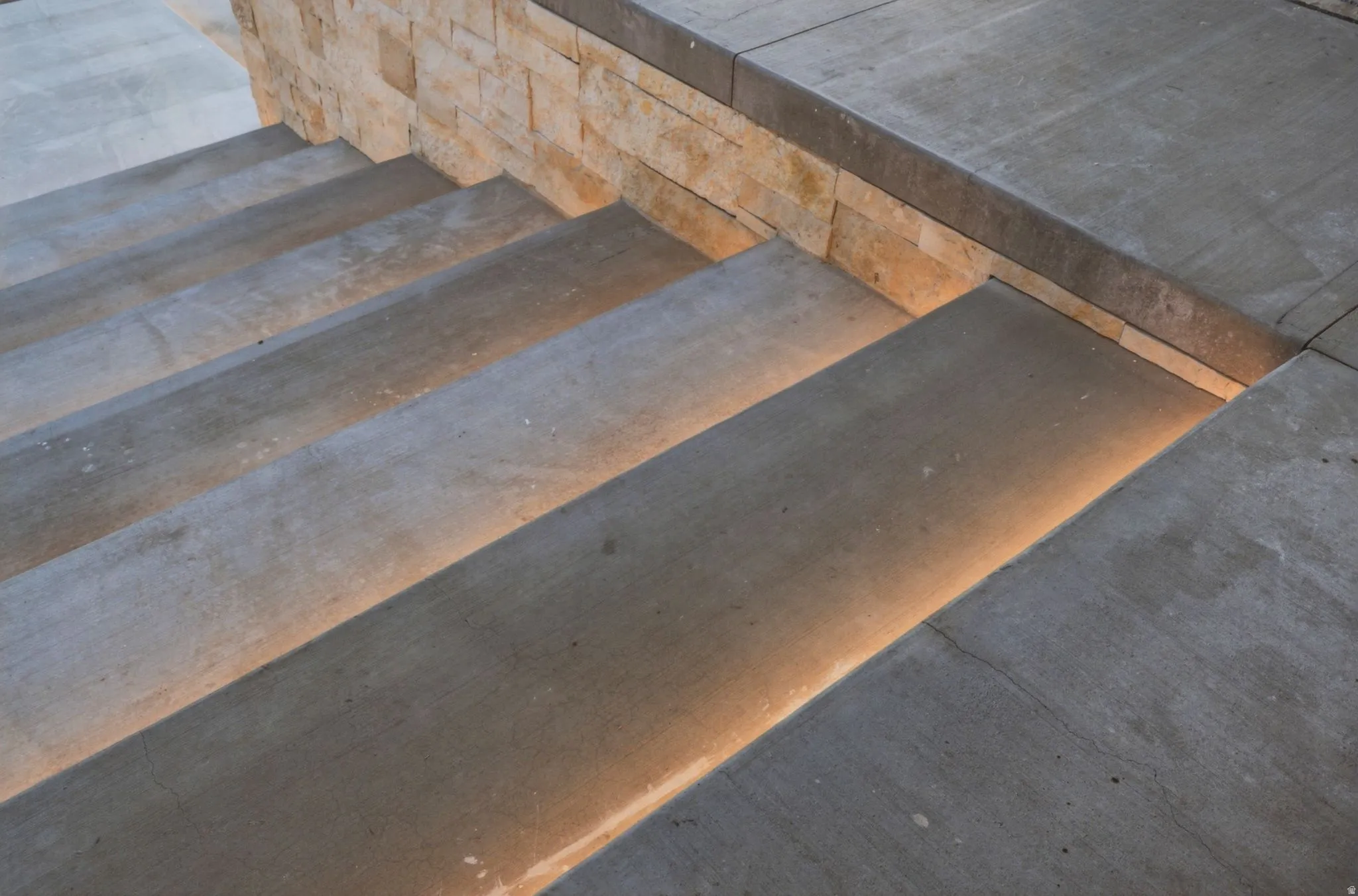 Concrete steps featuring integrated tread lighting and a stacked stone wall