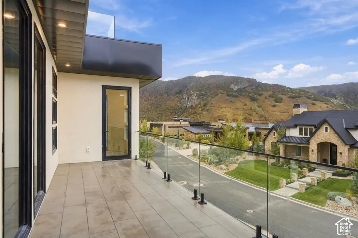 Covered balcony featuring large-format tile flooring, frameless glass railing, and mountain backdrop