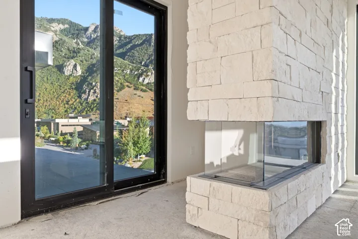 Floor-to-ceiling stone-clad fireplace featuring a glass-enclosed firebox and expansive sliding glass doors with mountain scenery