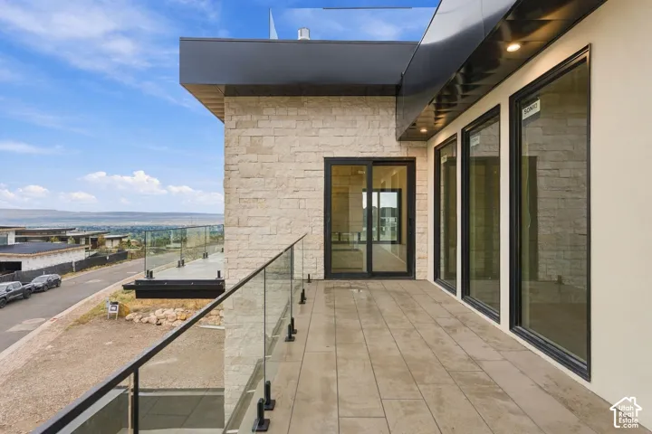 Exterior balcony featuring a stacked stone facade, tile flooring, glass panel railing with black hardware, and large-format black-frame windows and sliding glass doors