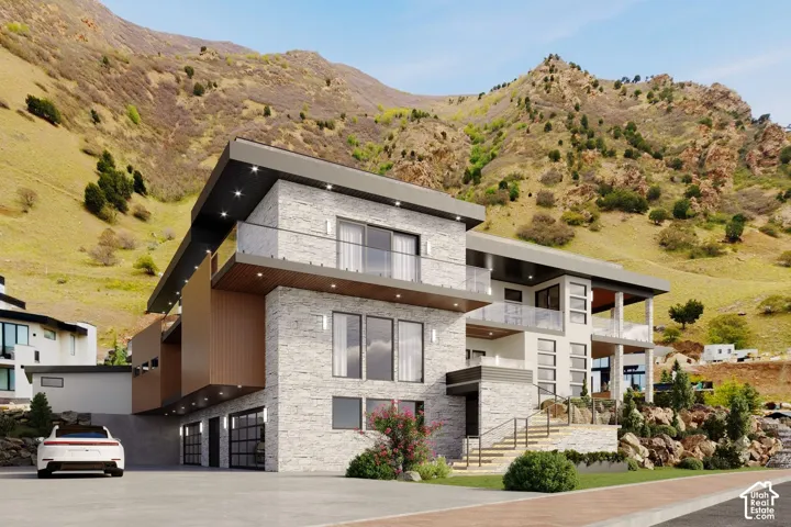 Modern architecture featuring stone and wood-finish paneling, glass balcony railings, a two-car garage, and a prominent mountain backdrop