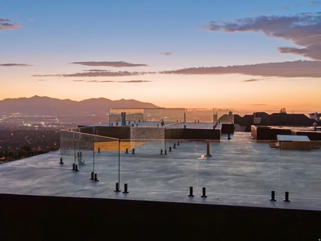 Rooftop terrace featuring glass railings, mountain scenery, and distant city lights