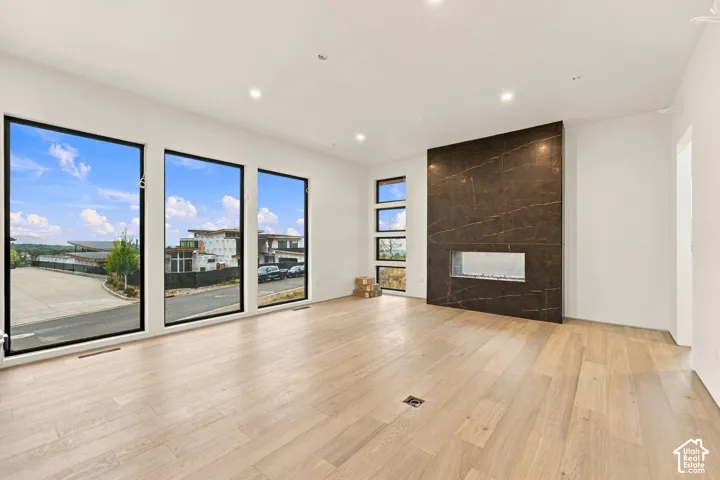 Open-concept interior featuring wood-finish flooring, floor-to-ceiling windows with black frames, recessed ceiling lighting, and a full-height stone fireplace surround