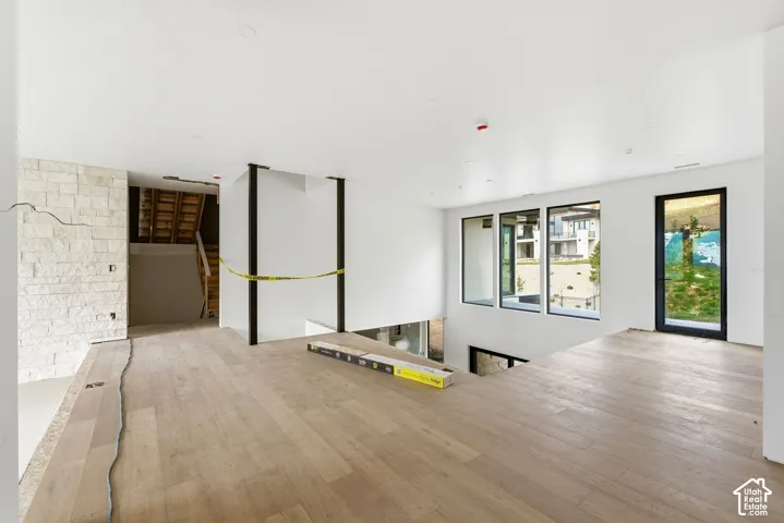 Open-concept interior featuring light wood-finish flooring, a textured stone accent wall, recessed lighting, expansive windows, and a black-framed glass entry door