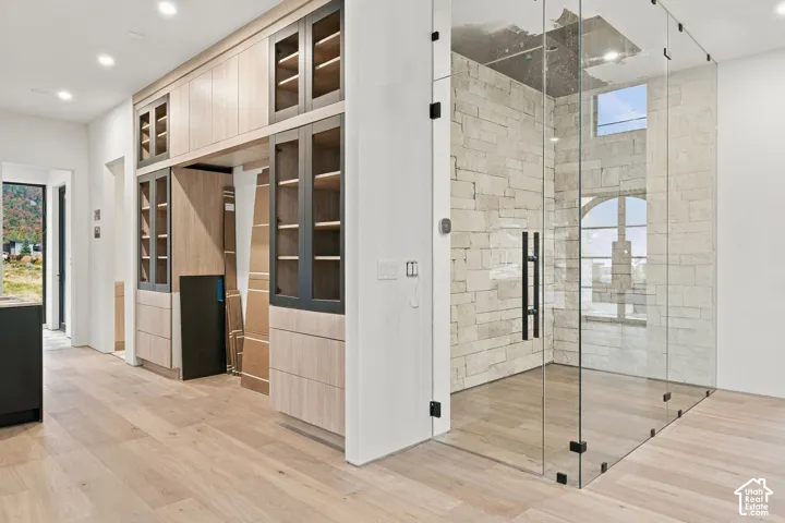 Floor-to-ceiling glass-enclosed shower featuring stone wall cladding and wood-finish flooring, complemented by built-in cabinetry with glass-front display panels and recessed ceiling lighting