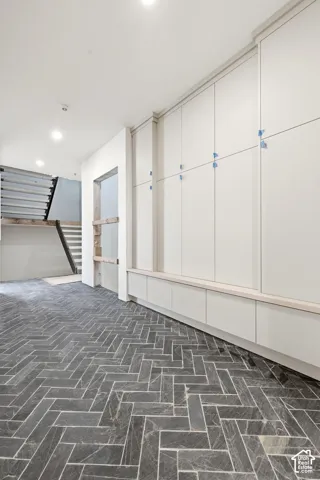 Full-height cabinetry with integrated bench seating, herringbone-patterned stone flooring, and recessed ceiling lighting
