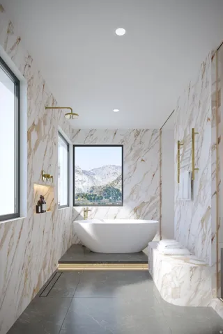 Freestanding soaking tub with mountain scenery, floor-to-ceiling marble-finish wall paneling, recessed wall niche, and large format floor tiling