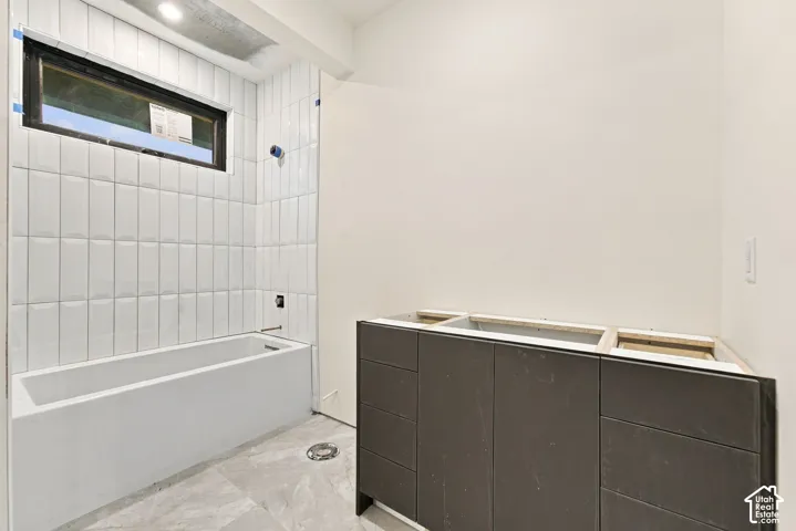 Bathroom featuring a built-in bathtub, floor-to-ceiling vertical subway tile surround, clerestory window, and a dark-finish double vanity cabinet