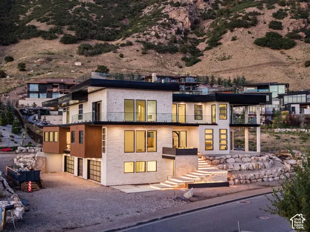 Contemporary architecture with a light-colored stone exterior, expansive glass windows, multiple balconies with glass railings, and a tiered rock retaining wall