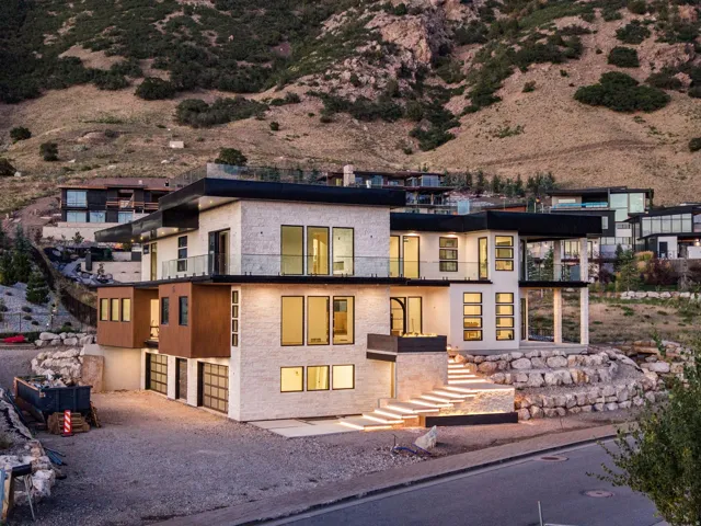 Contemporary architecture with a light-colored stone exterior, expansive glass windows, multiple balconies with glass railings, and a tiered rock retaining wall