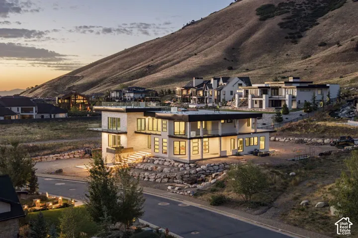 Modern multi-level exterior featuring stone cladding, extensive glass paneling, flat roof architecture, glass-railed balconies, and natural rock landscaping