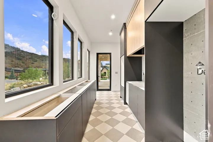 Contemporary interior featuring custom cabinetry with a two-tone matte charcoal and light wood finish, large-format floor-to-ceiling windows, diamond-patterned tile flooring, a textured concrete accent wall, and mountain landscape imagery