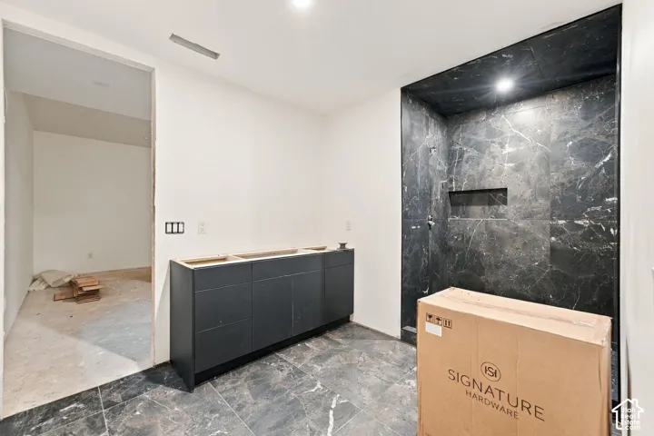Bathroom featuring dark stone-finish flooring and wall tile, a walk-in shower enclosure with a built-in recessed wall niche, and a matte dark cabinetry vanity