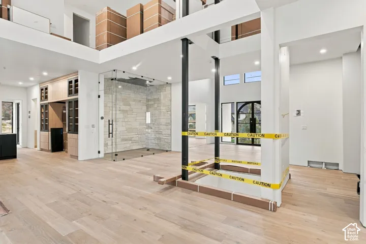 Open-concept interior featuring light wood-finish flooring, floor-to-ceiling glass-enclosed shower with stone-tile surround, dual-level mezzanine, and recessed lighting