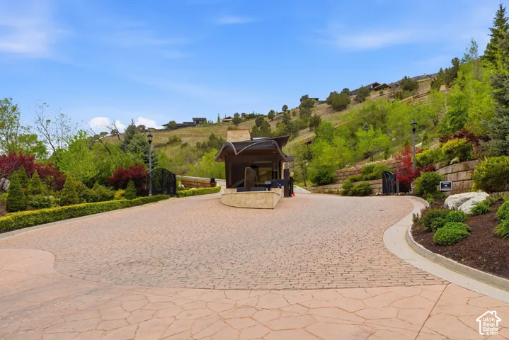 Stone paver driveway with integrated landscaping, gated entry, and a guardhouse structure