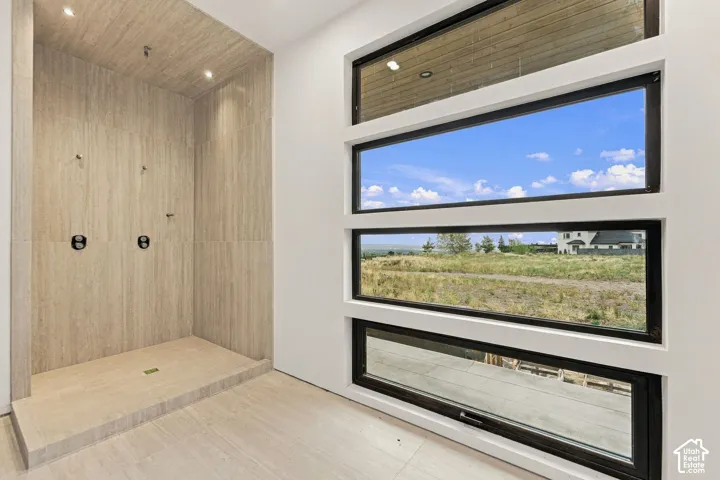 Walk-in shower featuring floor-to-ceiling stone-finish tile, dual wall-mounted shower heads, recessed ceiling lighting, and a bank of four horizontal black-framed windows