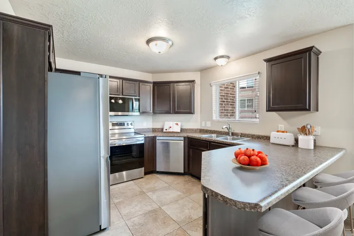 Kitchen featuring dark wood-finish cabinetry, stainless steel appliances, a double basin sink, and a counter-height breakfast bar. *Virtually staged photo.