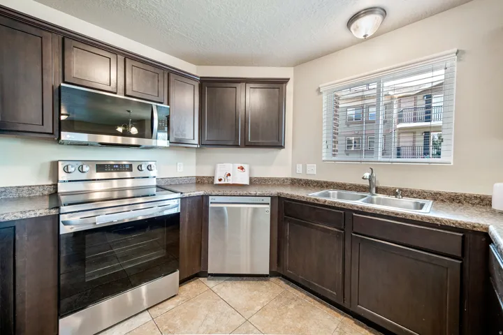Kitchen with dark wood cabinetry, stainless steel appliances, dual basin sink, tile flooring, and a window with blinds. *Virtually staged photo.