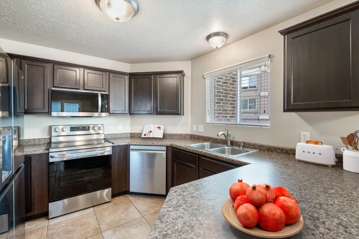 Kitchen featuring dark wood-finish cabinetry, stainless steel appliances, speckled countertops, and tile flooring. *Virtually staged photo.