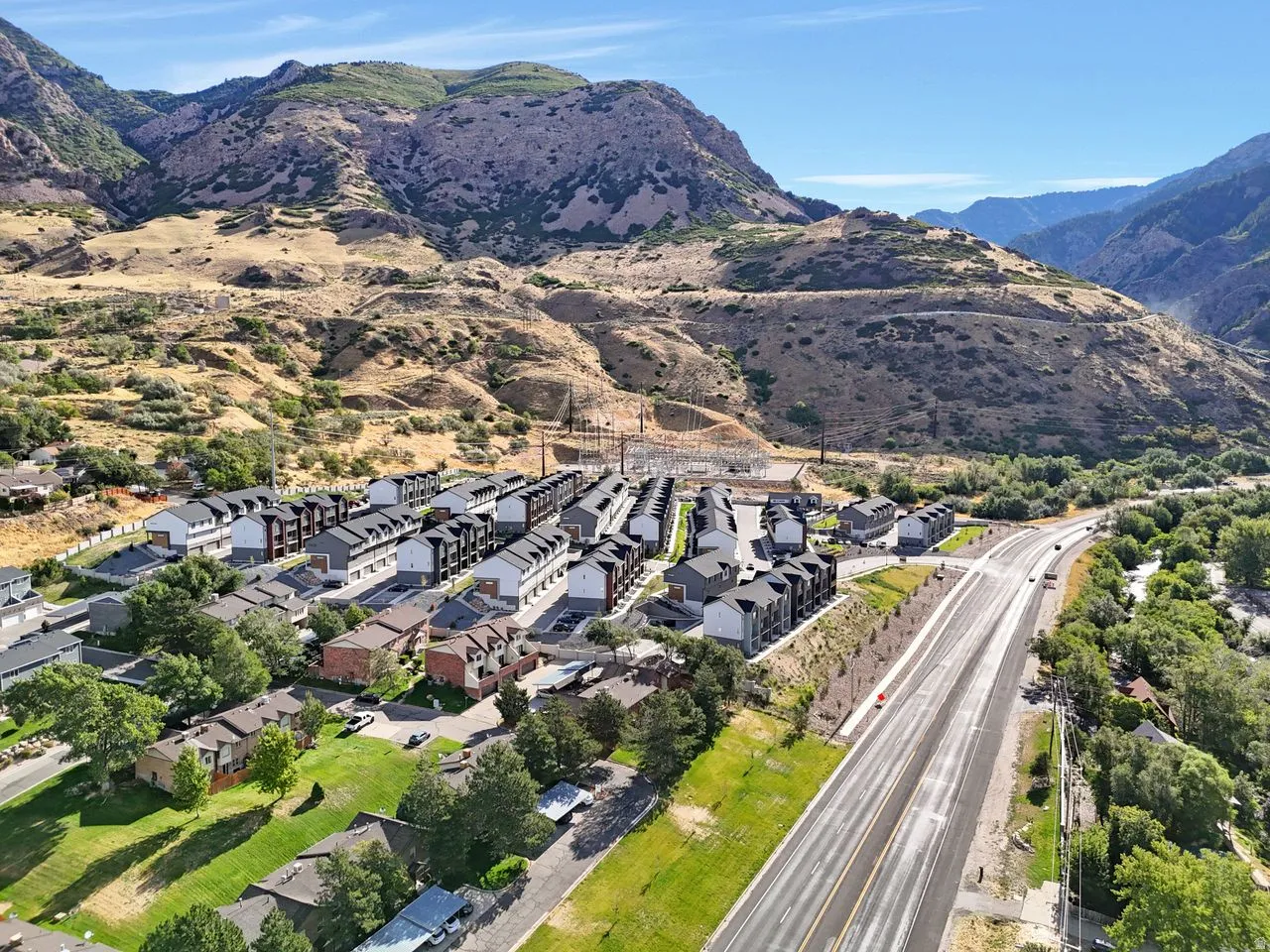 Mountainous backdrop, residential development, established landscaping, paved road access, and a clear sky