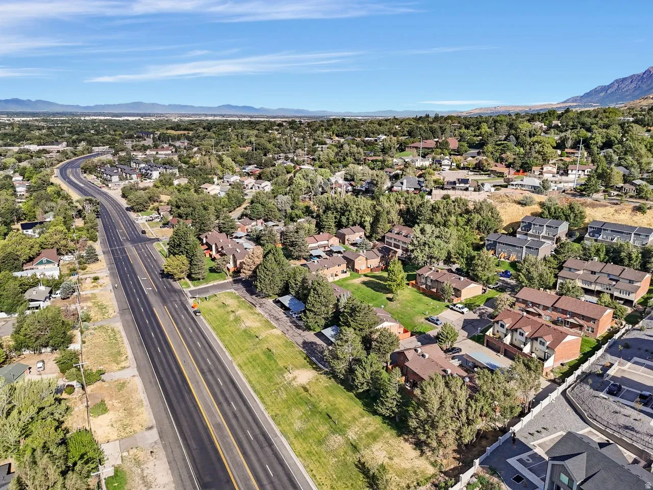 Expansive aerial perspective showcasing a residential area with varied housing styles, mature trees, and a prominent multi-lane roadway