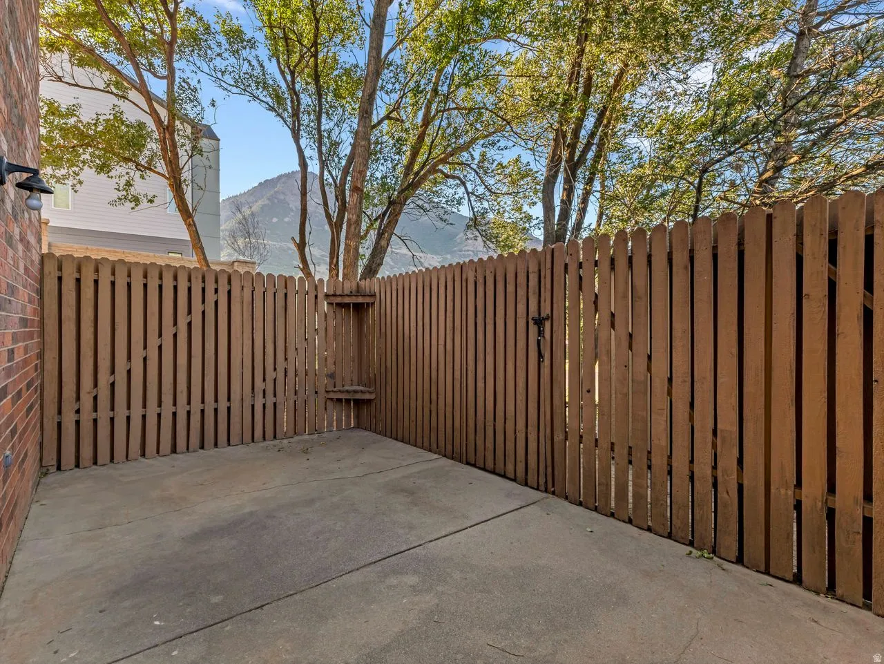 Private fenced patio space with a concrete slab, wood privacy fence, and brick exterior wall with an exterior light fixture