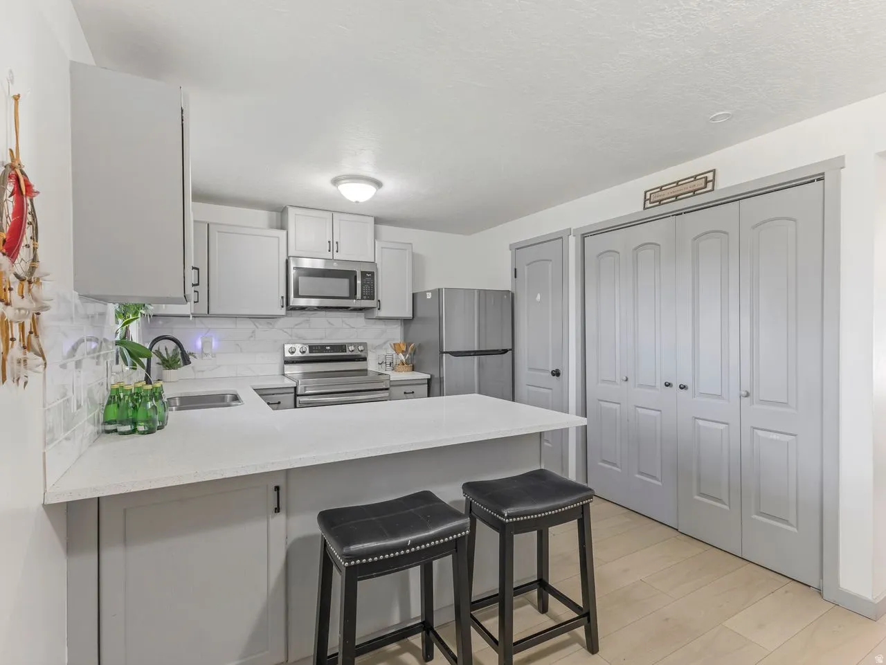 White countertops, undermount sink, stainless steel appliances, white subway tile backsplash, and light wood-finish flooring