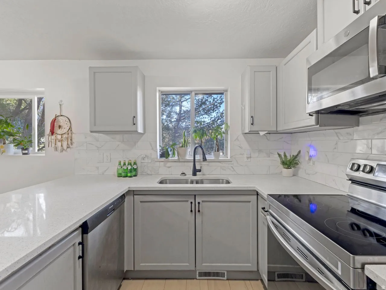 U-shaped kitchen featuring light gray cabinetry, light-toned countertops, a stainless steel sink with a black gooseneck faucet, a subway tile backsplash, and a built-in microwave