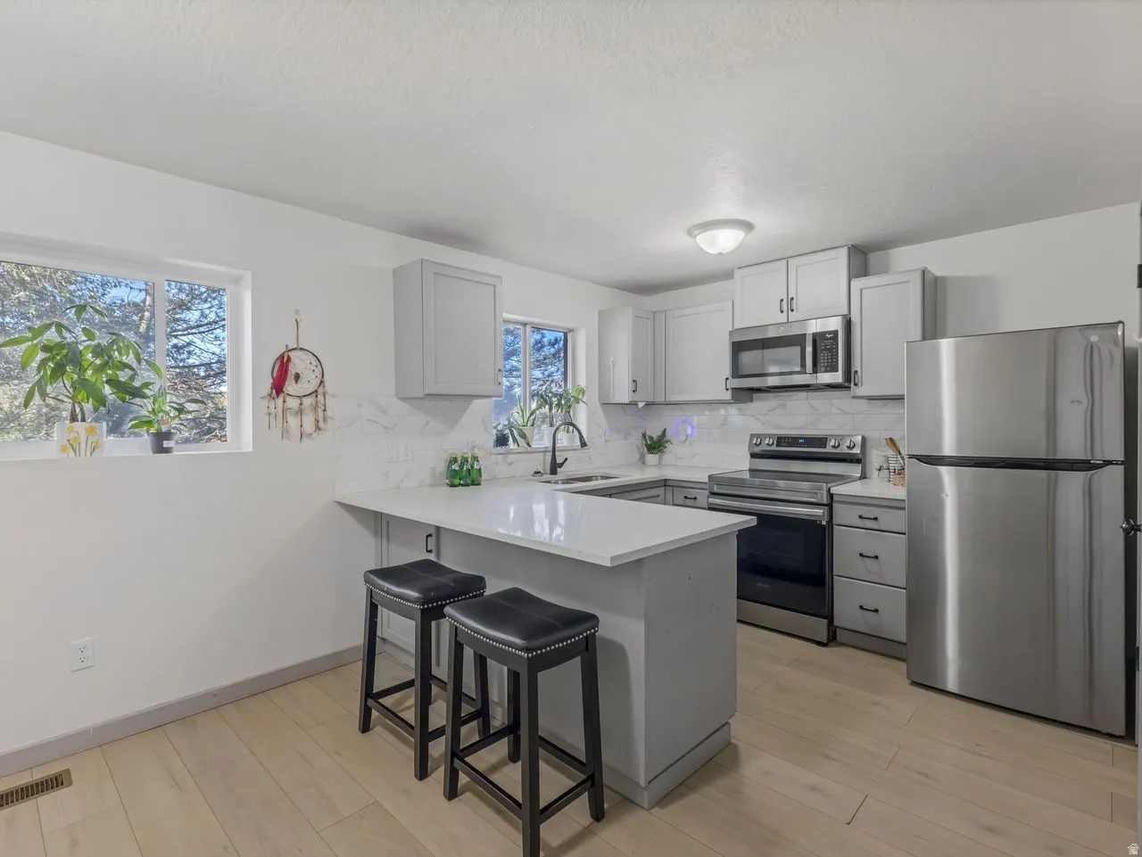 Kitchen featuring light wood-finish flooring, white countertops, stainless steel appliances, and gray shaker-style cabinetry