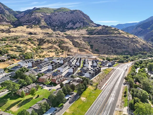 Mountainous backdrop, residential development, established landscaping, paved road access, and a clear sky