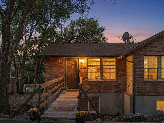 Brick exterior, wood entry ramp with railings, transom window above entry, multiple windows with blinds, pitched shingle roof