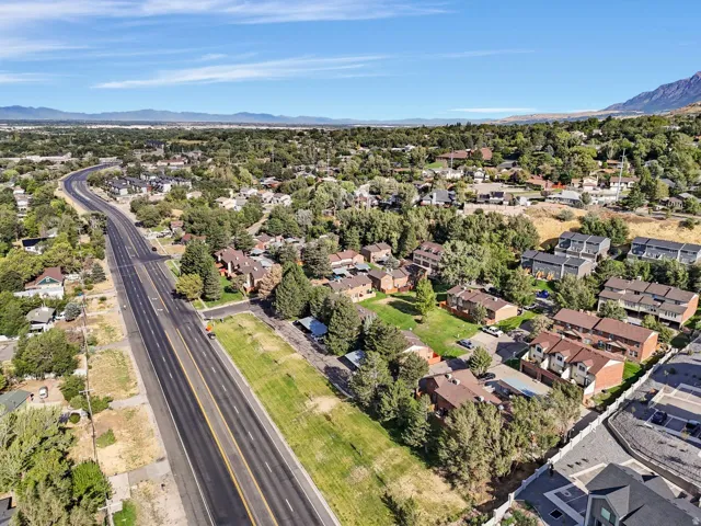 Expansive aerial perspective showcasing a residential area with varied housing styles, mature trees, and a prominent multi-lane roadway