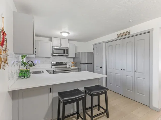 White countertops, undermount sink, stainless steel appliances, white subway tile backsplash, and light wood-finish flooring