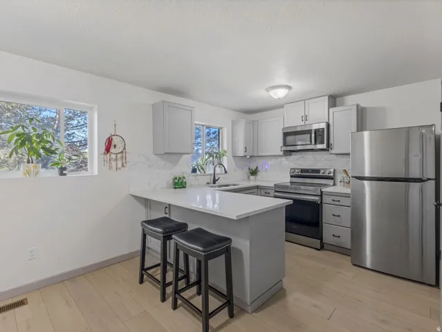Kitchen featuring light wood-finish flooring, white countertops, stainless steel appliances, and gray shaker-style cabinetry