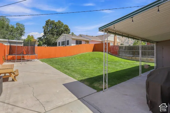 Expansive concrete patio with a covered section, mature landscaping, and a vibrant privacy fence