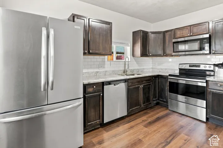 Kitchen featuring stainless steel appliances, dark wood-finish cabinetry, white subway tile backsplash, light-toned countertops, and wood-finish flooring