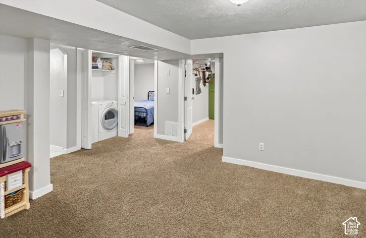 Carpeted living area with light gray walls, white trim, and a built-in laundry closet with a stackable washer