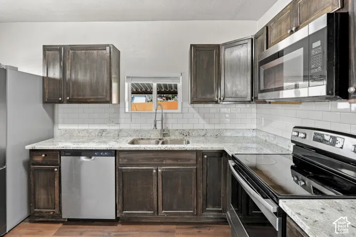 Kitchen featuring dark wood-finish cabinetry, light stone countertops, white subway tile backsplash, and stainless steel appliances
