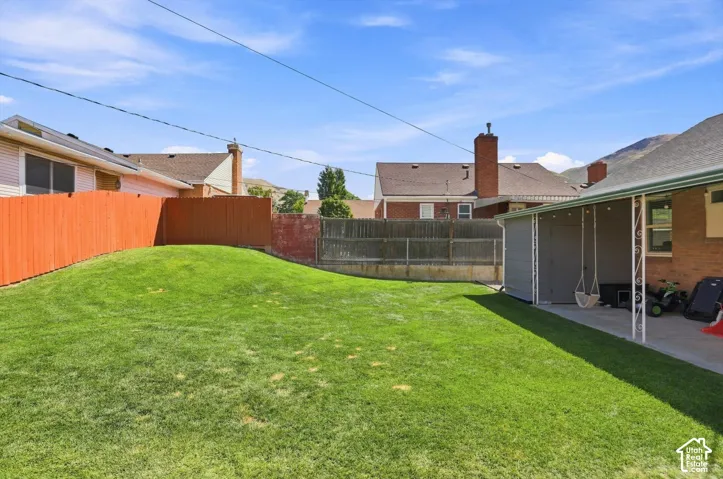 Expansive lawn area with a sloped grade, privacy fencing, a covered patio, and attached storage structure