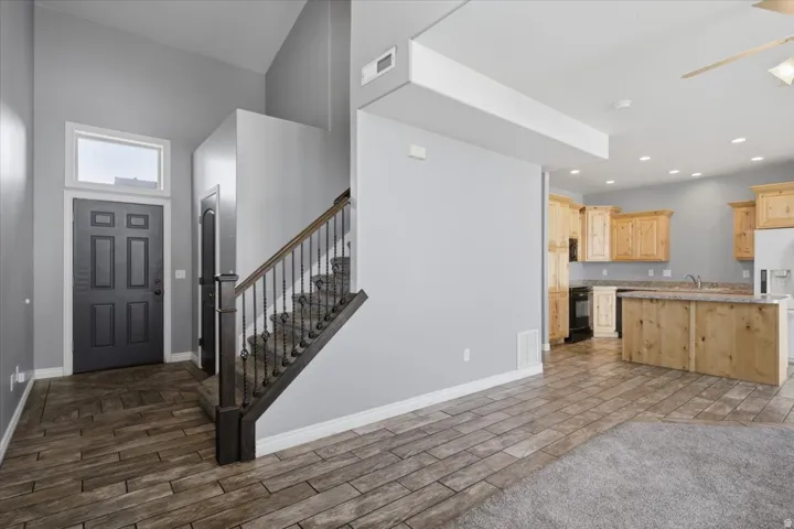 Vaulted entryway with transom window, wood-finish flooring, staircase with wrought iron balusters, and a kitchen featuring light wood cabinetry